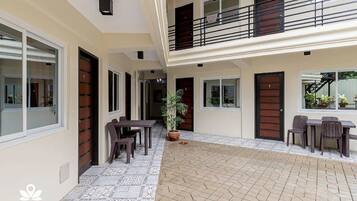 Un edificio residencial de varios niveles con un patio cubierto, mobiliario exterior y plantas en macetas.