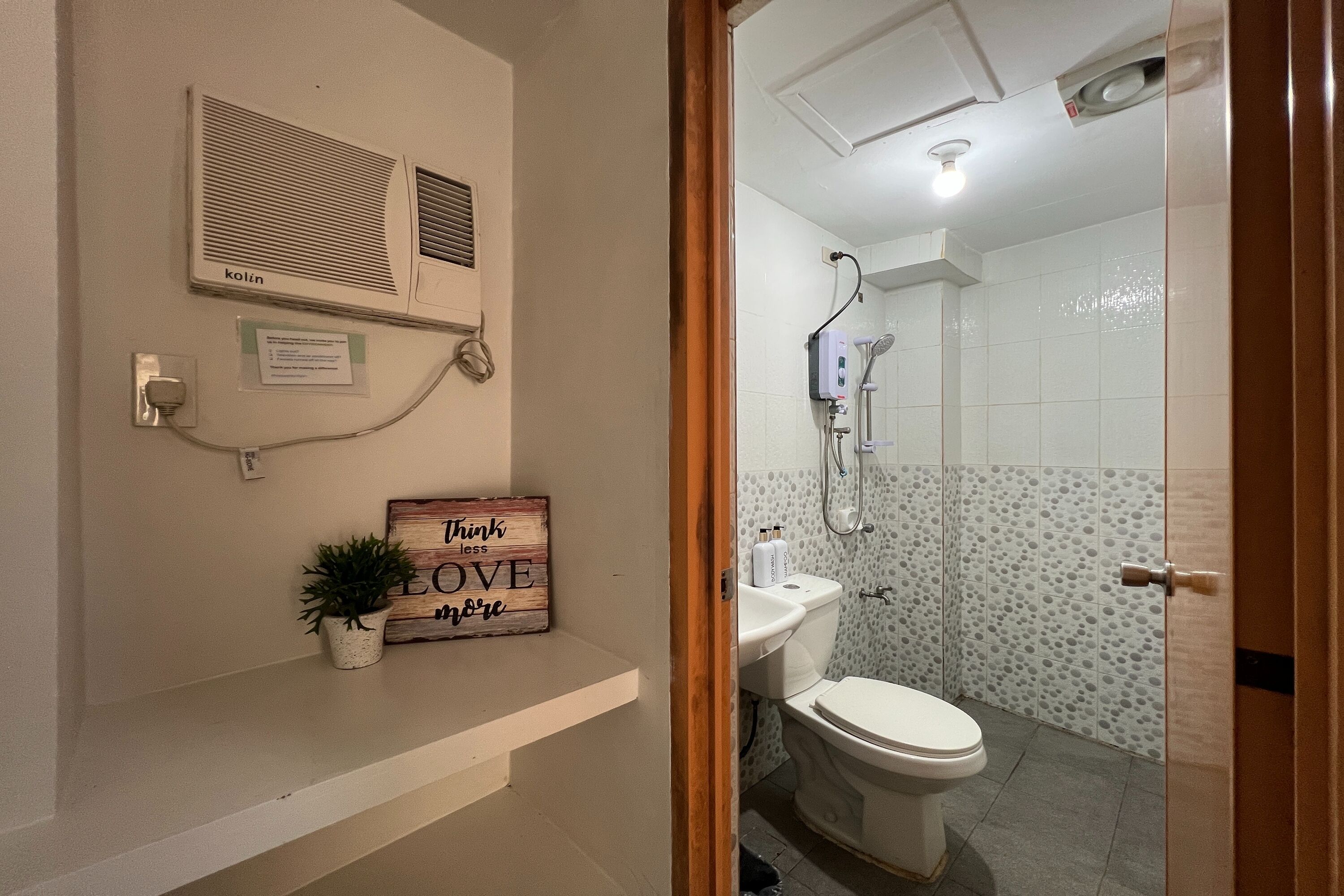 A bathroom with a toilet, shower, and a wall-mounted air conditioner.