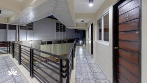 Un pasillo de hotel con una escalera, un balcón con plantas y una puerta numerada con el número 12.
