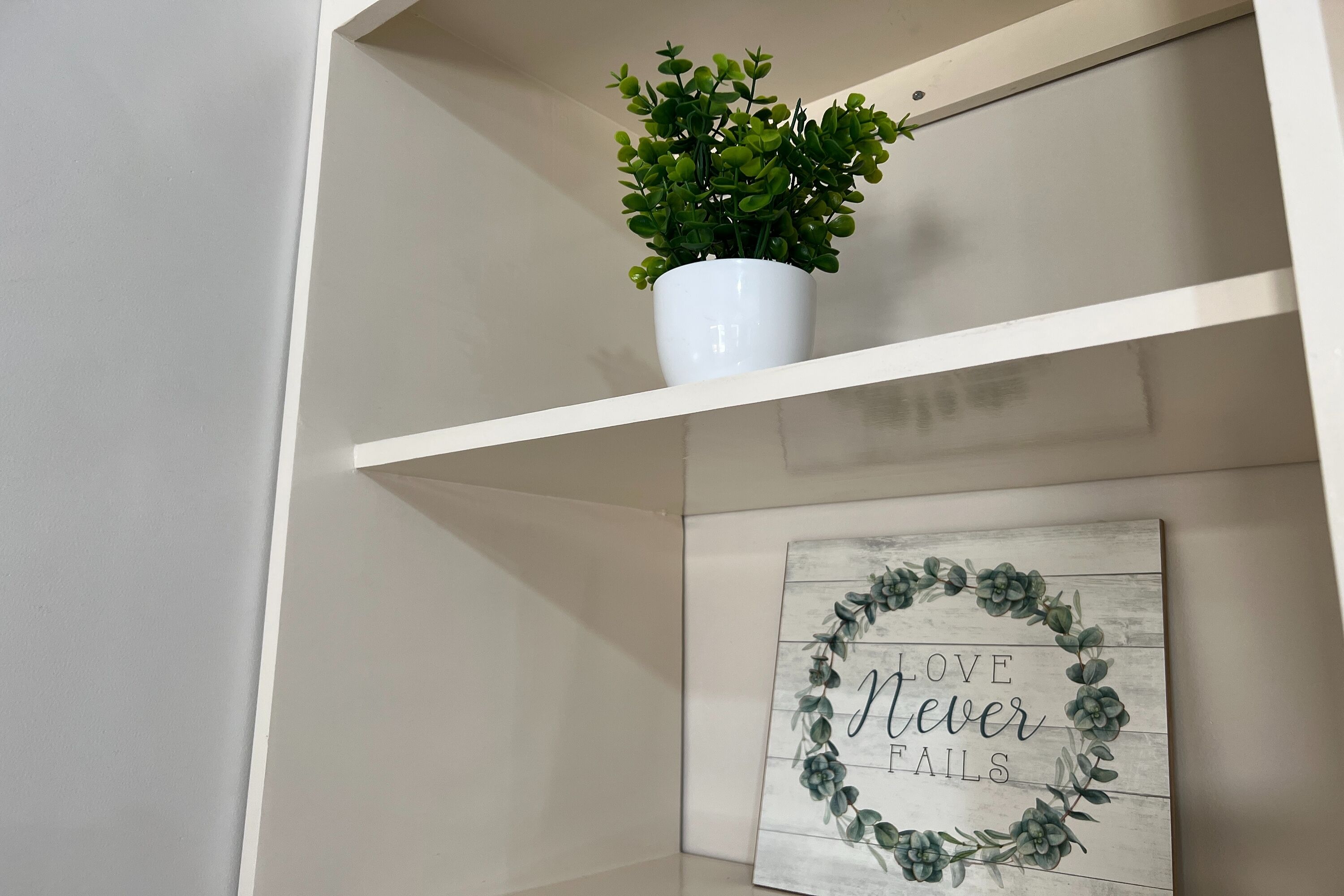 A shelf with a potted plant and a framed sign with the text "LOVE NEVER FAILS".