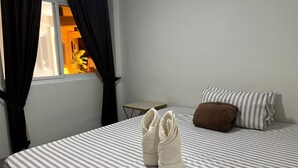 Habitación de hotel con cama, ropa de cama a rayas, almohada marrón y un par de pantuflas blancas sobre la cama.