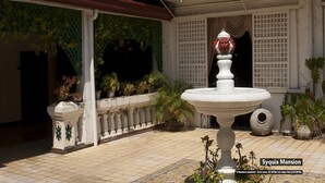 Un patio con una fuente, plantas en macetas y suelo de baldosas.