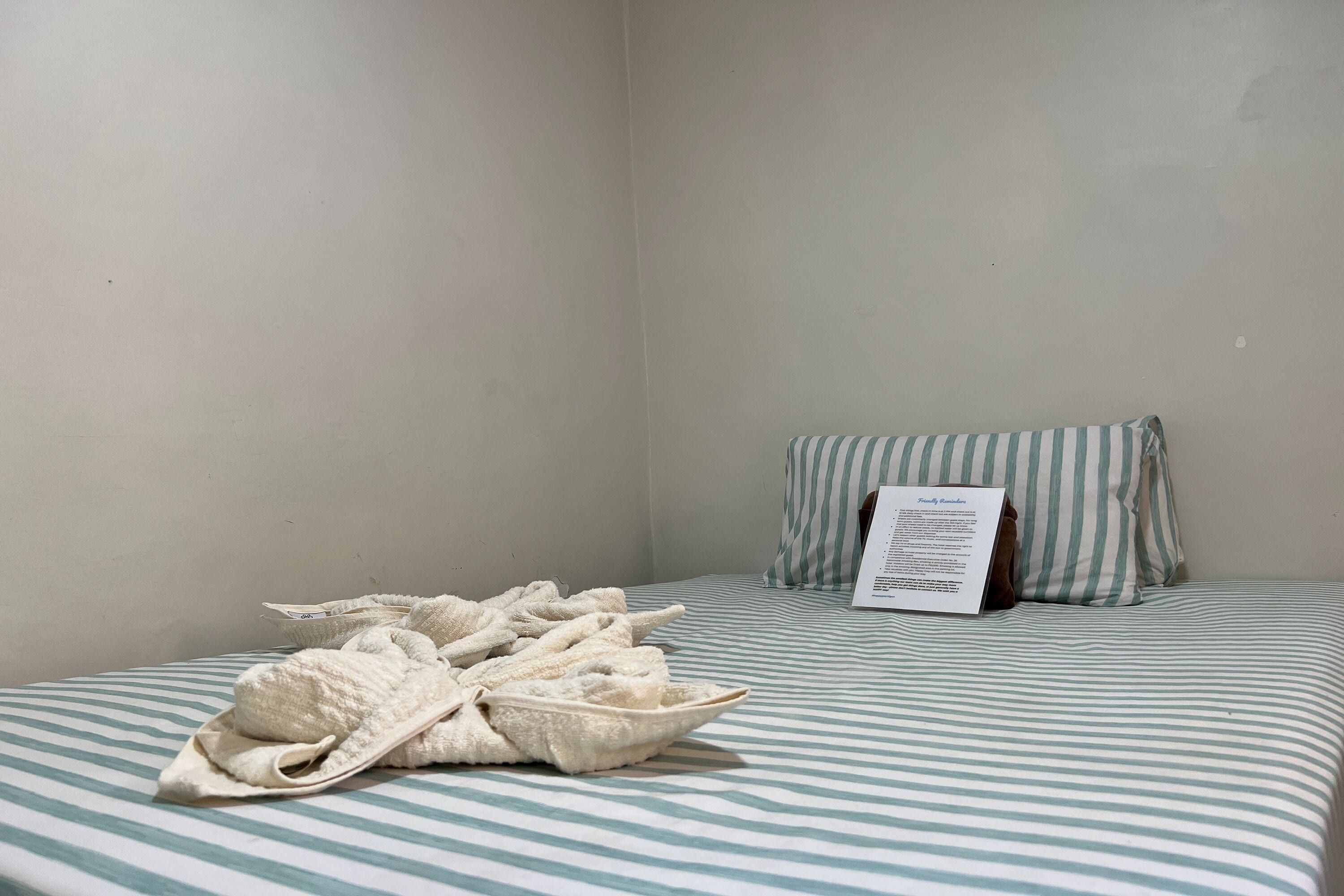 Une chambre avec un lit recouvert d’une courtepointe à rayures, un oreiller avec une taie d’oreiller à rayures et une serviette pliée posée sur le lit.