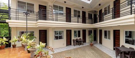 A multi-level hotel atrium with a central courtyard, potted plants, and outdoor seating areas.