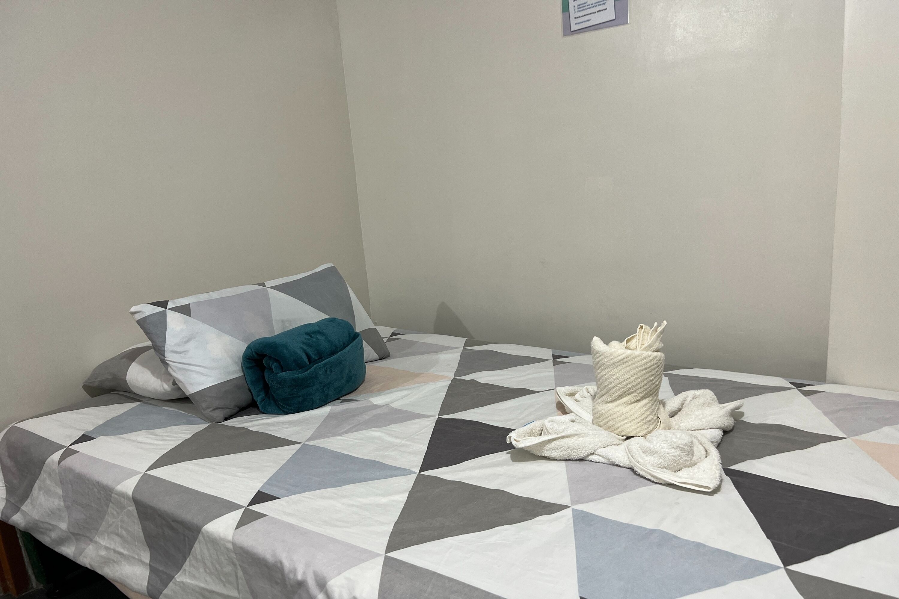A neatly made bed with a geometric patterned bedspread, a teal pillow, and a white towel bundle.