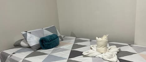 A neatly made bed with a geometric patterned bedspread, a teal pillow, and a white towel bundle.