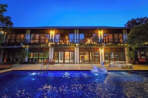 Un hotel con piscina, un flotador con forma de cisne y una fachada iluminada al anochecer.