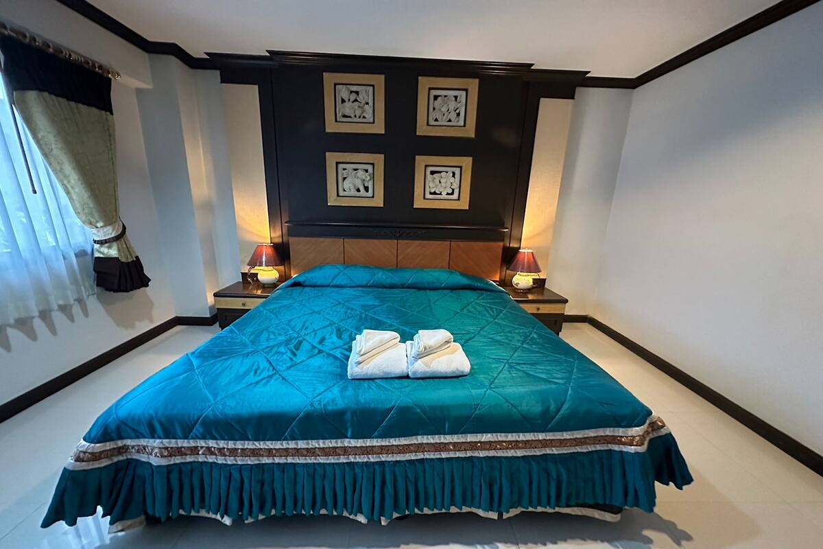 A neatly made bed with a teal bedspread, two bedside lamps, and a headboard with four framed pictures.