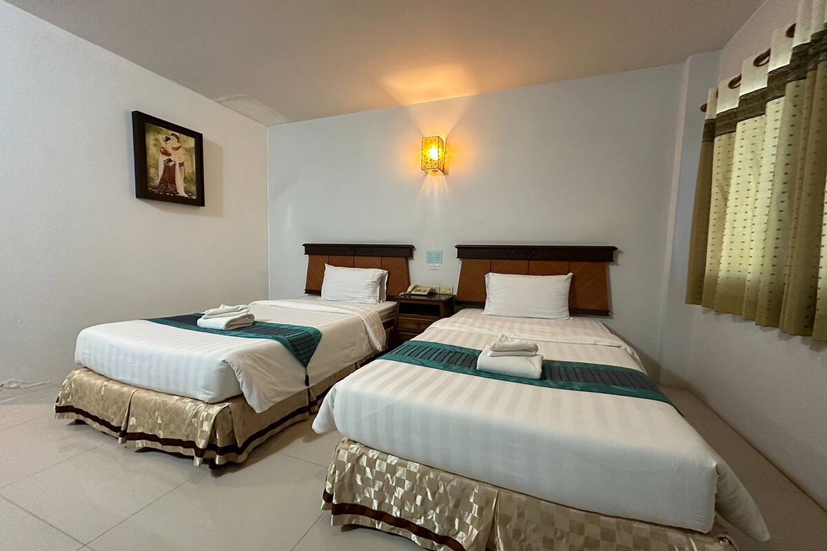 A hotel room with two beds, a nightstand with a phone, a wall-mounted light, and a painting on the wall.