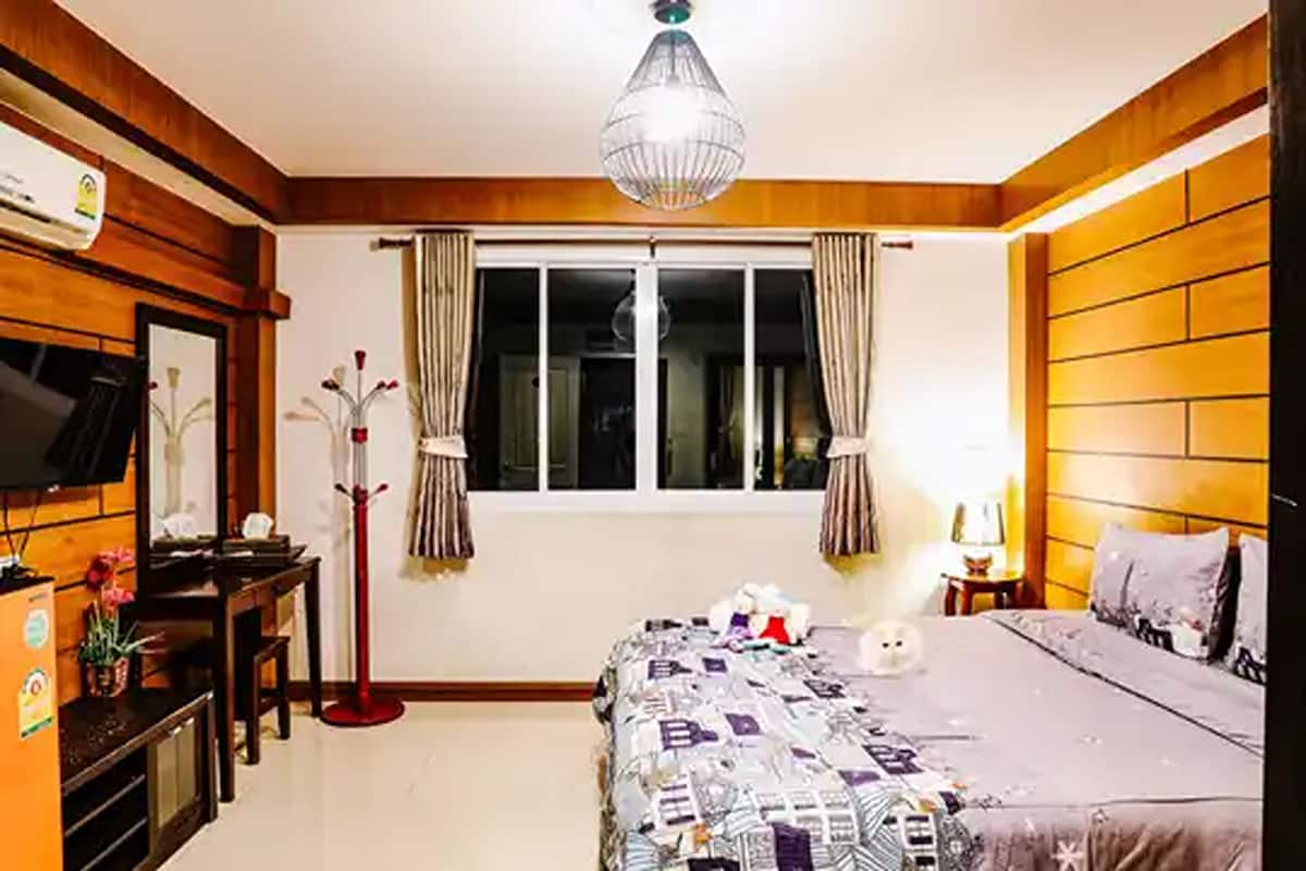 A bedroom with a bed, a desk, a television, and a window with curtains.