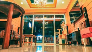 A spacious lobby with a high ceiling, a chandelier, and a large window with a view of the outside. - Sleep Hotel (Chonburi)