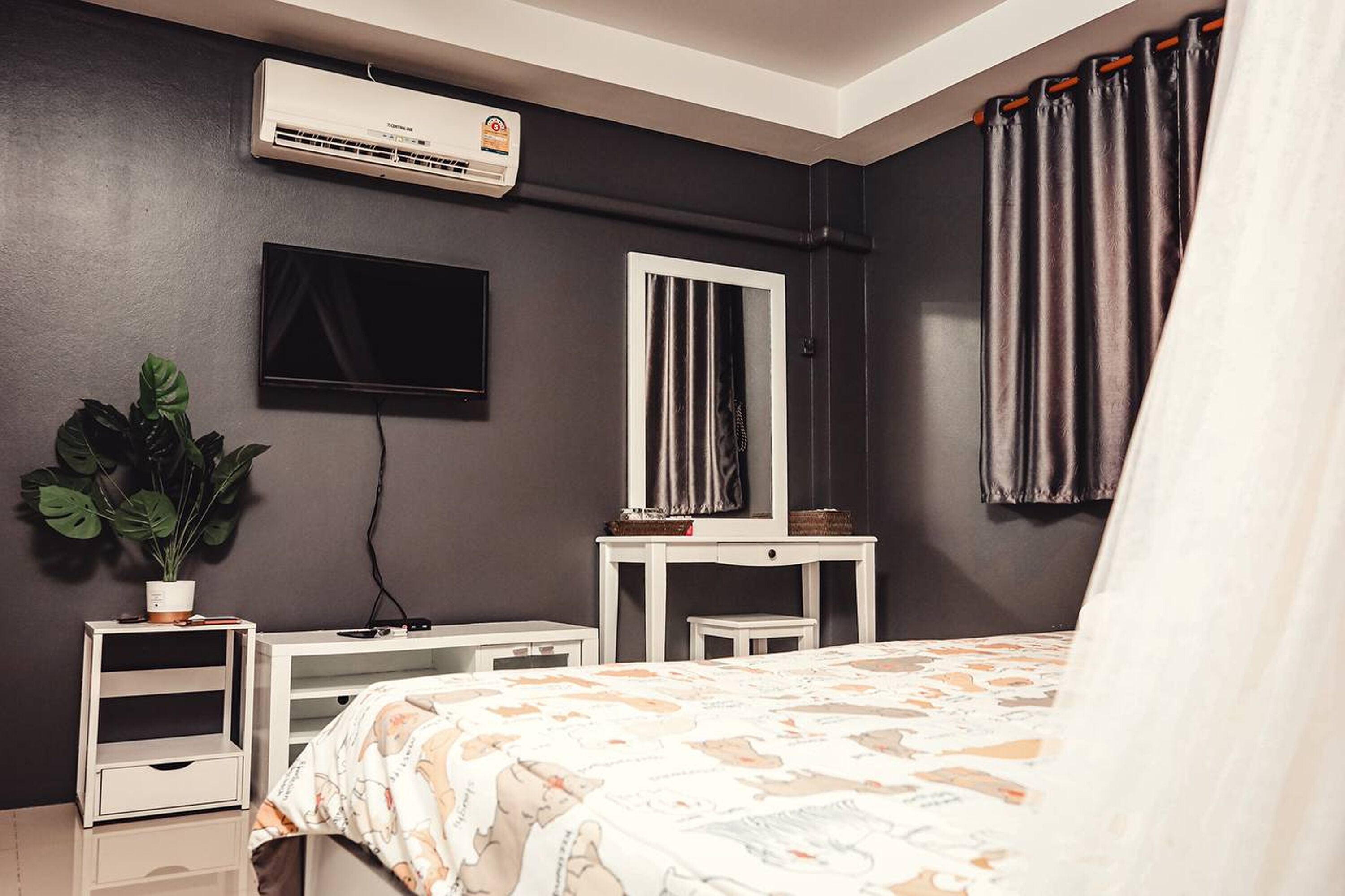 Quarto com cama, televisão, espelho, planta em vaso e ar-condicionado fixado na parede.