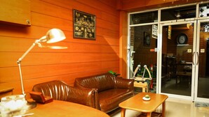 A room with a brown leather sofa, a wooden coffee table, and a desk with a lamp. There is a large window with a view of the street and a sign that reads "SLEEP HOTEL." - Sleep Hotel (Chonburi)