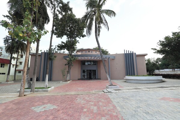 A building with a modern entrance, palm trees, and a paved walkway.