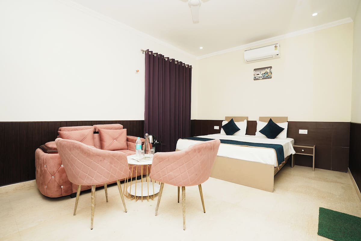 A hotel room with a bed, a small table with chairs, a sofa, and an air conditioning unit.