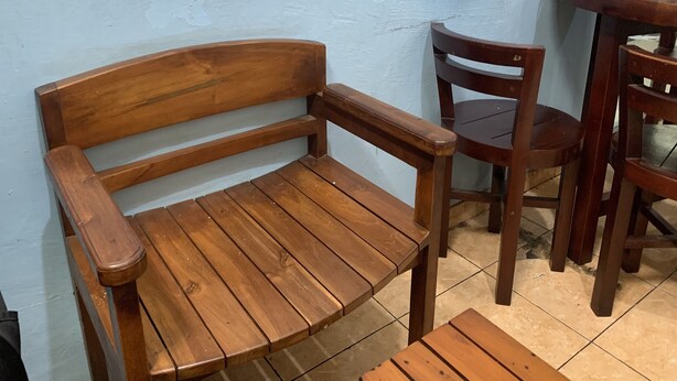 Una panca e una sedia in legno appoggiate a un muro, con un tavolo e altre sedie nelle vicinanze.
