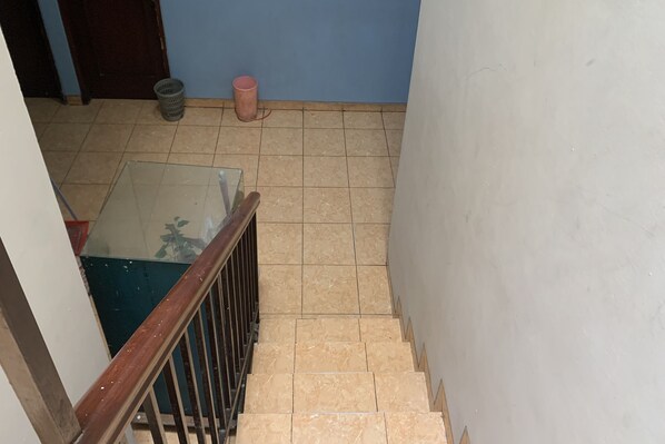 Un escalier recouvert de carreaux beiges, une main courante en bois et une table en verre au bas de l’escalier.