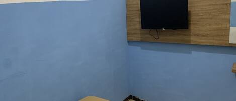 A room with blue walls, a wooden panel with a television mounted on it, and a beige floor.