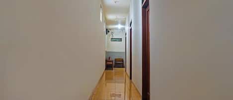 Un couloir avec un sol carrelé, des murs blancs et un ventilateur de plafond.