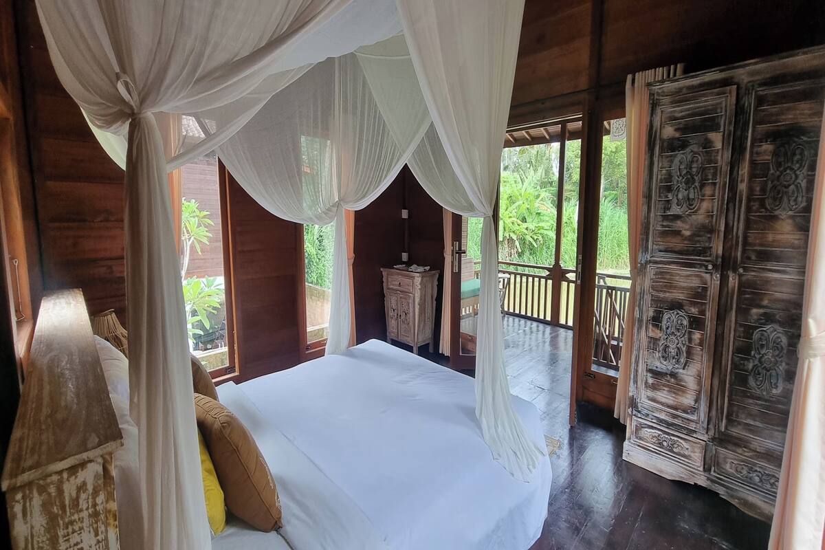 A room with a bed, a nightstand, a wardrobe, and a balcony with a railing.