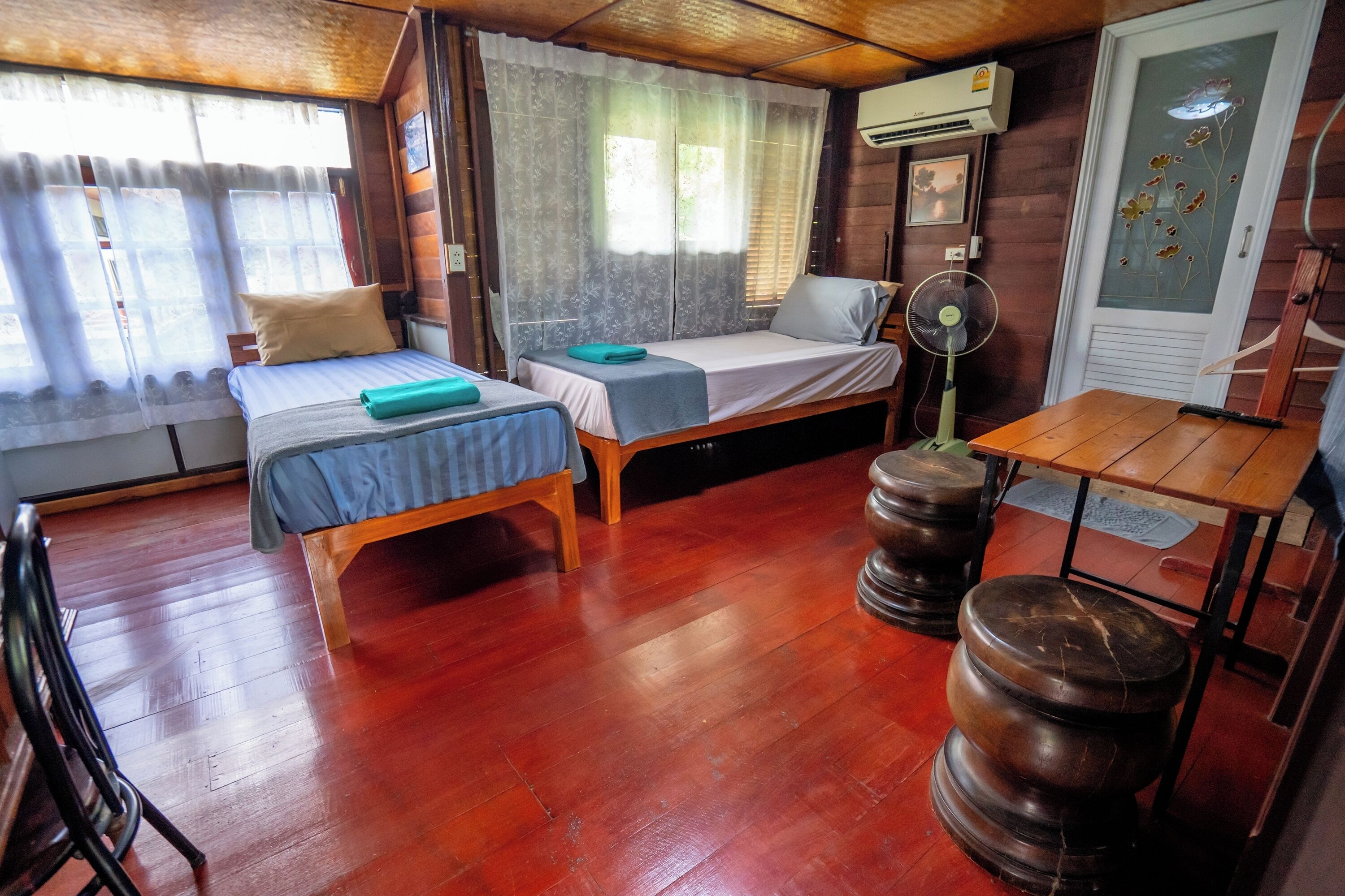 Una habitación con dos camas de madera, una mesa de madera, un ventilador y un barril de madera.