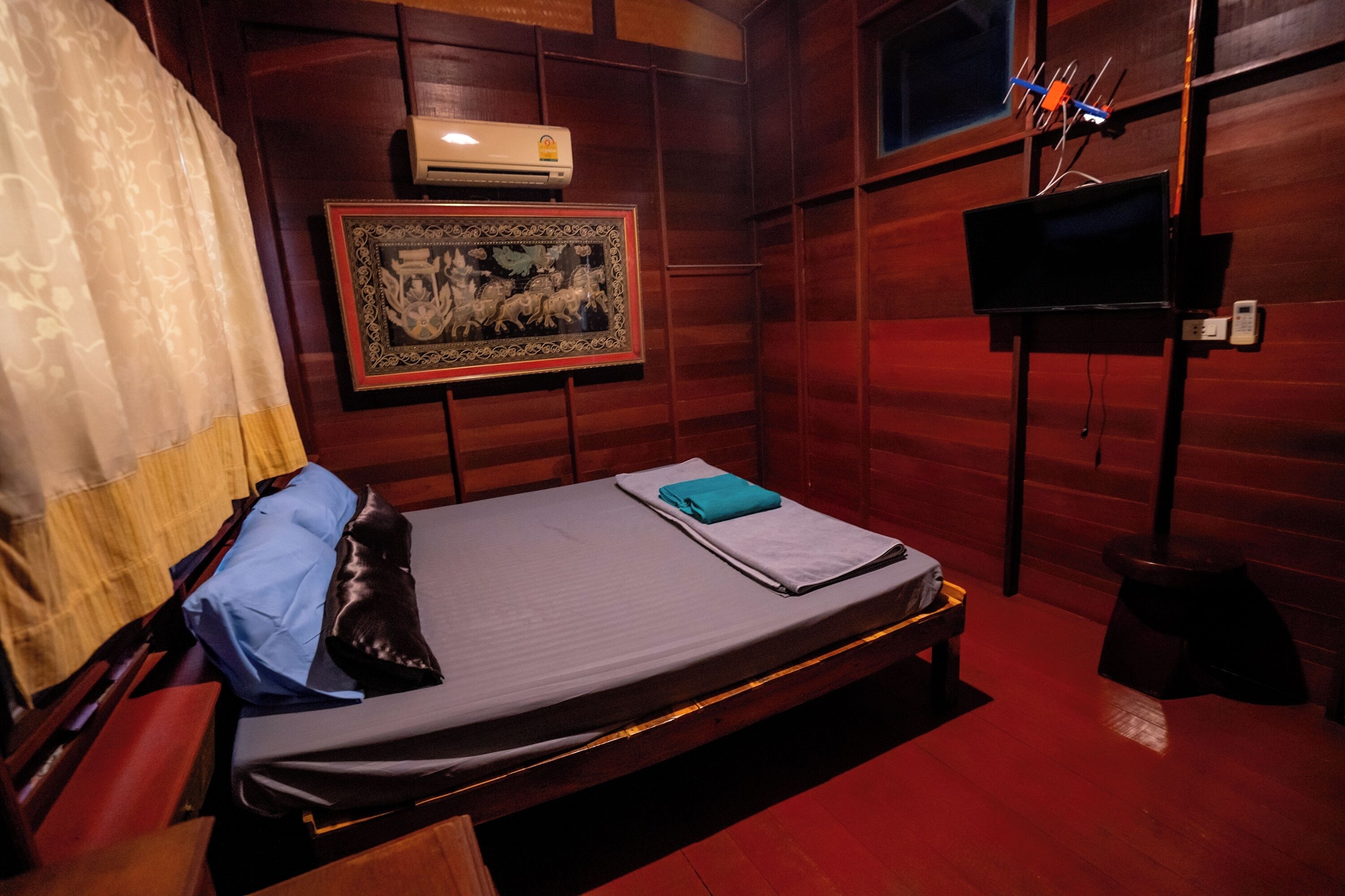 A room with a bed, a framed picture on the wall, an air conditioning unit, and a television on a stand.