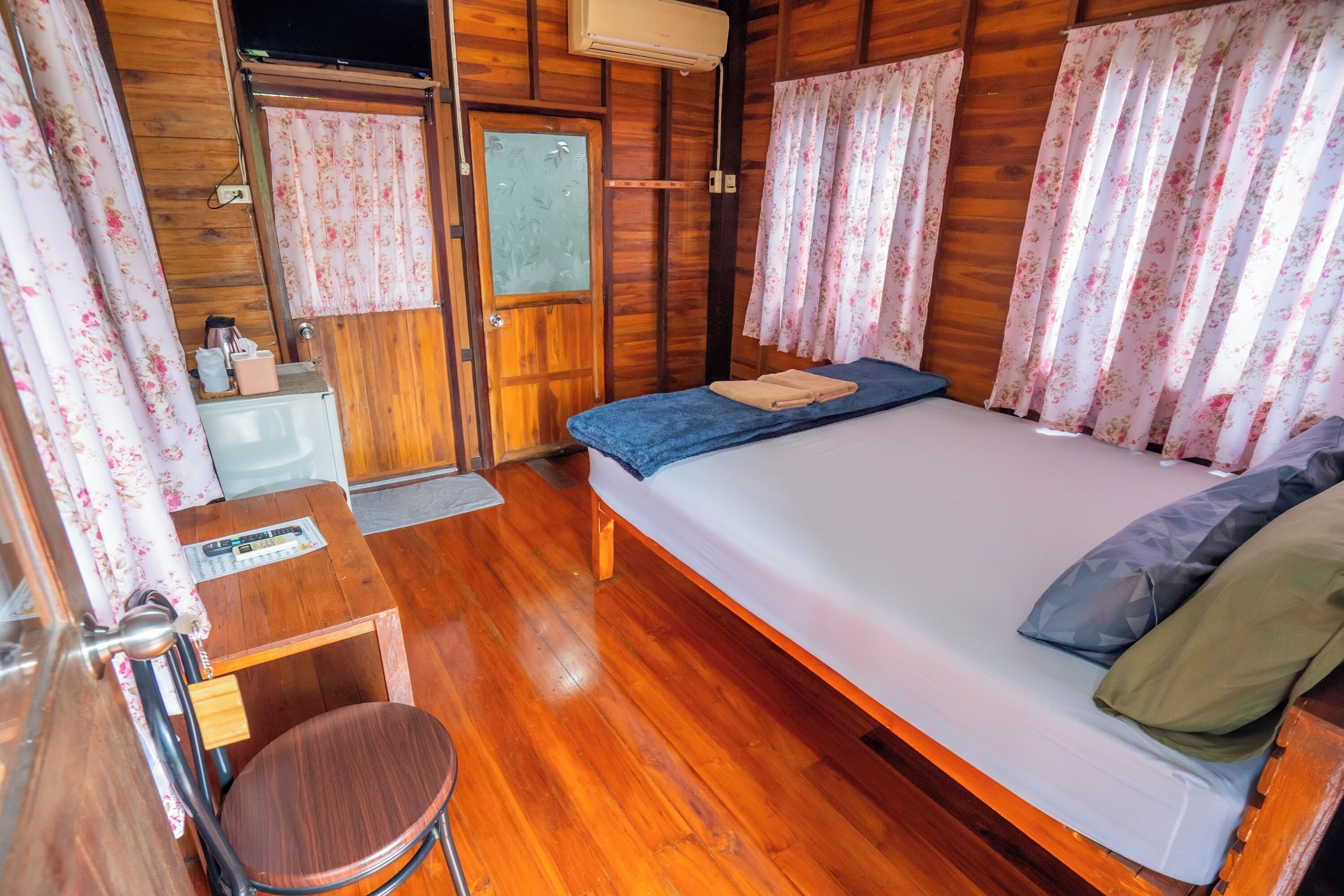 A wooden cabin bedroom with a bed, a small table, a chair, and a window with curtains.