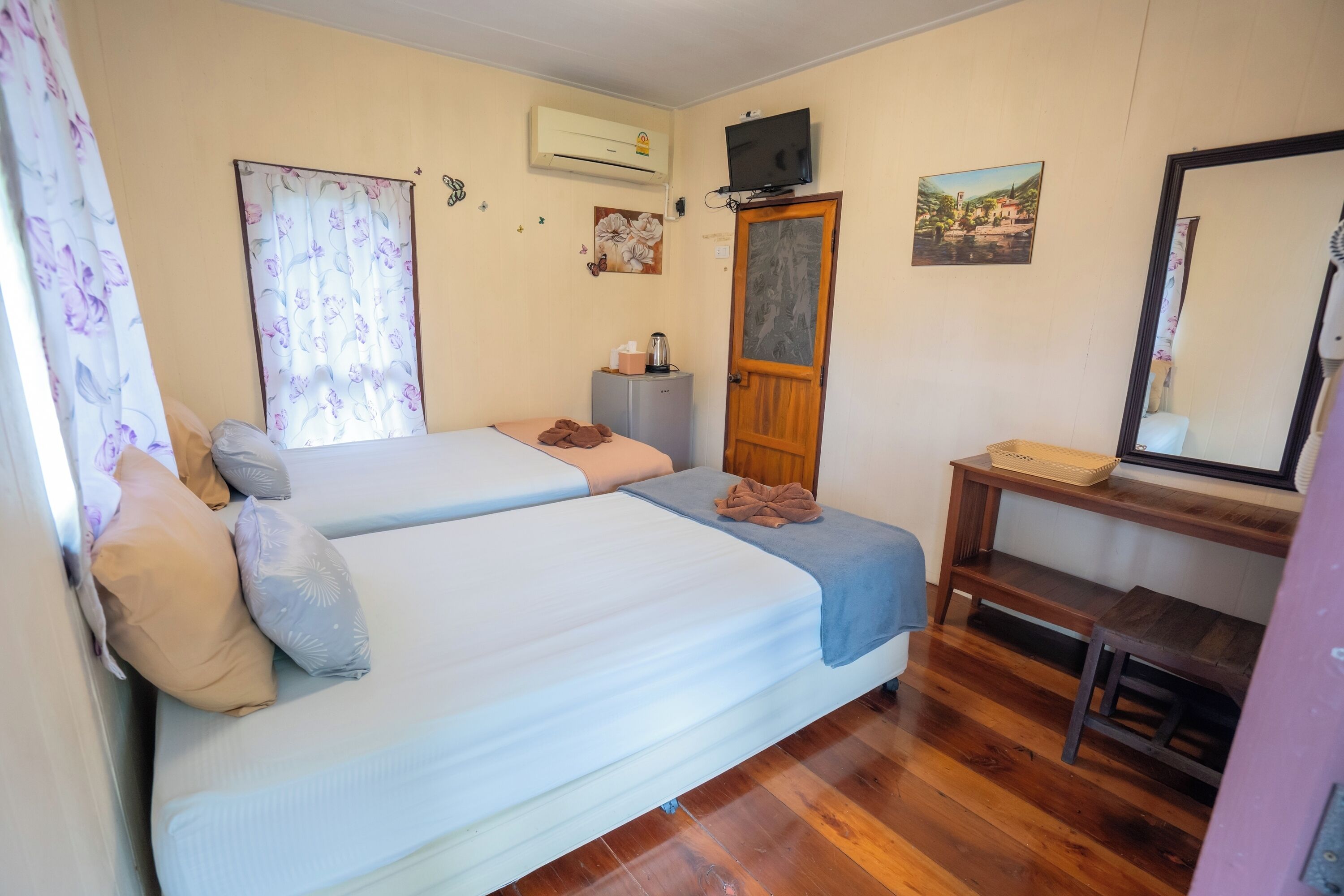 A bedroom with two beds, a wooden desk, a chair, an air conditioning unit, a television, and a small cabinet.