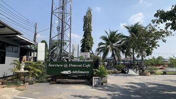 A sign for Seewiew @ Donwai Cafe with a view of the surrounding area including a palm tree, a statue, and a building with a metal roof.