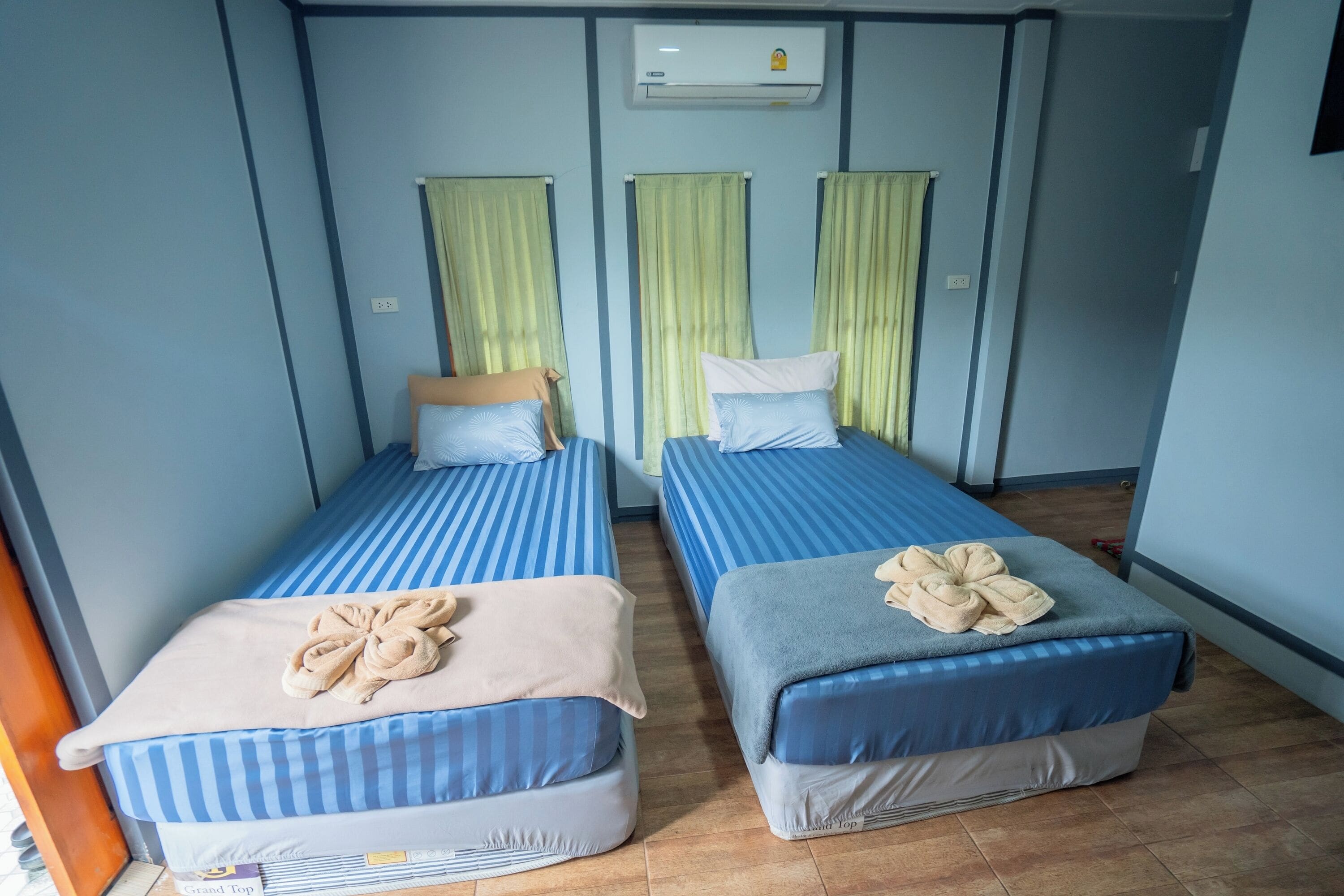 Dos camas individuales con ropa de cama a rayas, aire acondicionado en el techo y cortinas verdes.