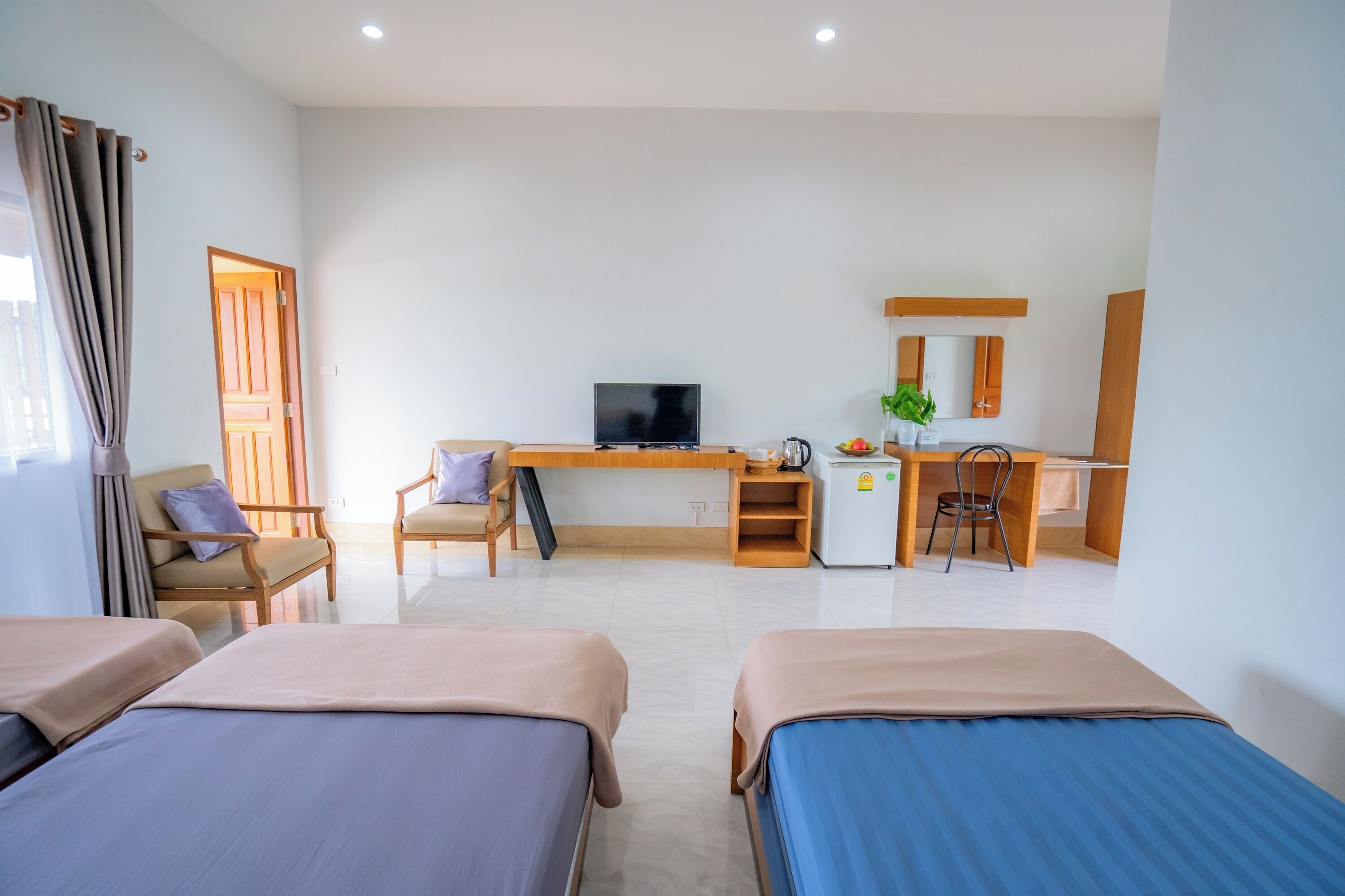 A hotel room with two beds, a desk, a television, a small refrigerator, and a chair.
