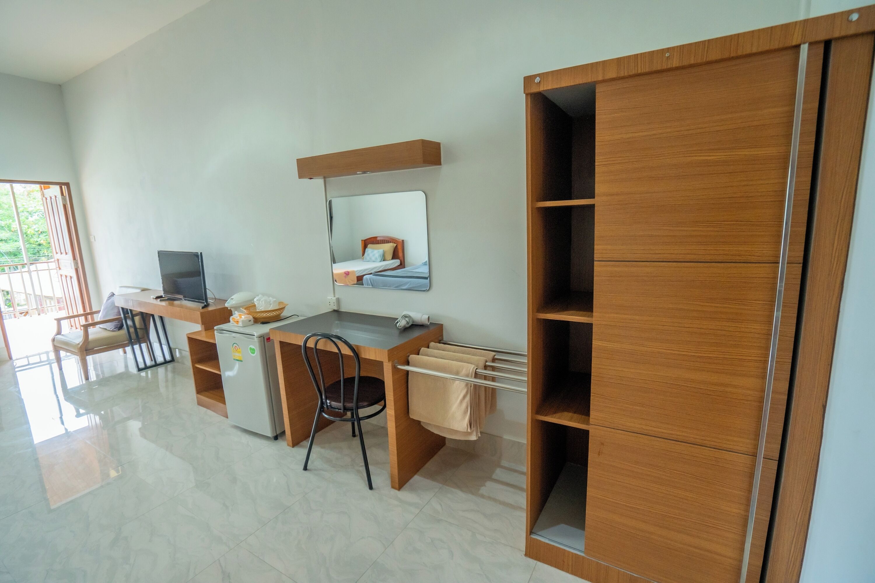 Habitació moderna amb escriptori de fusta, una cadira, nevera petita, mirall i armari.