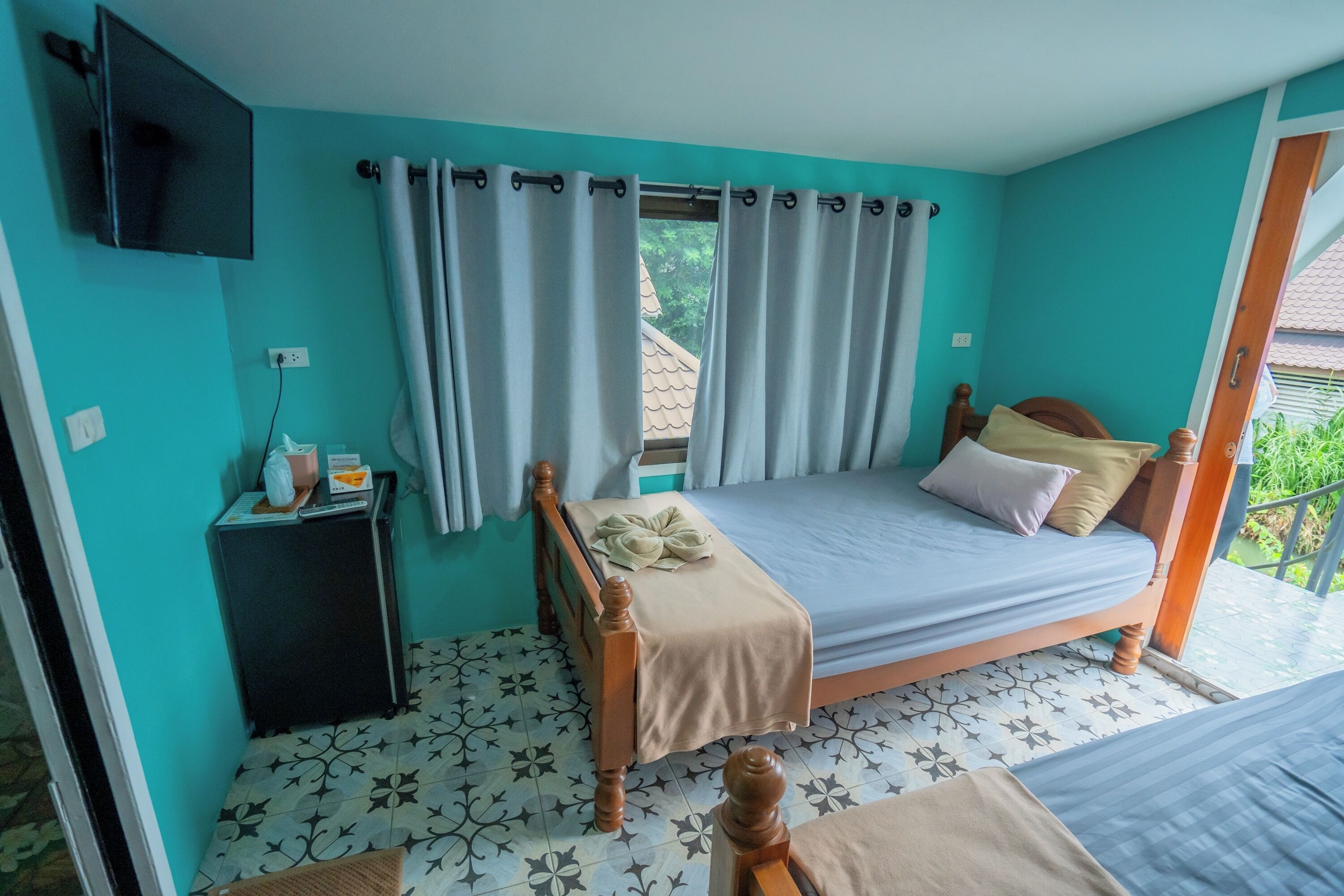 Un dormitorio con cama, cortinas, televisor, una mesita y una ventana con vistas a la vegetación.