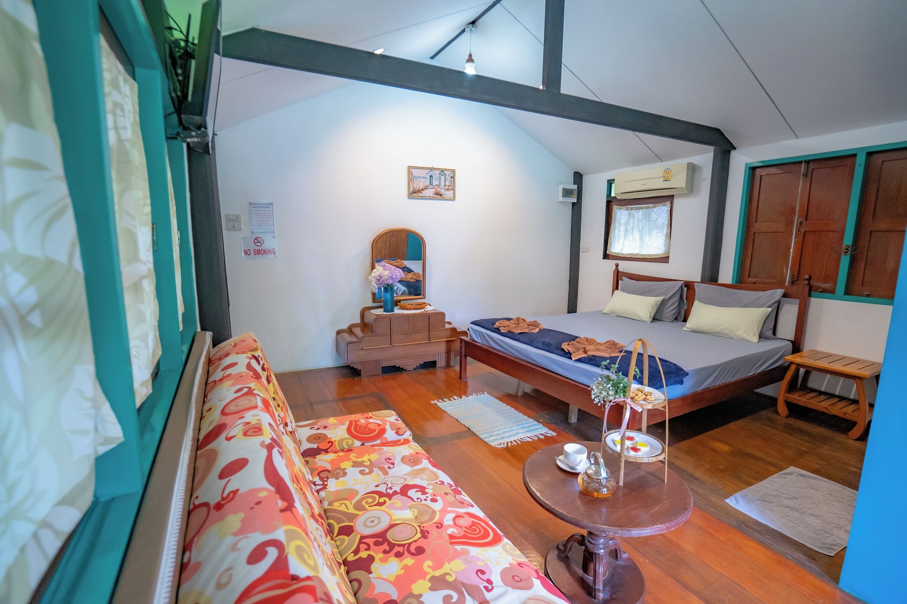 A room with a sofa, a bed, a small table with a tray, and a mirror.
