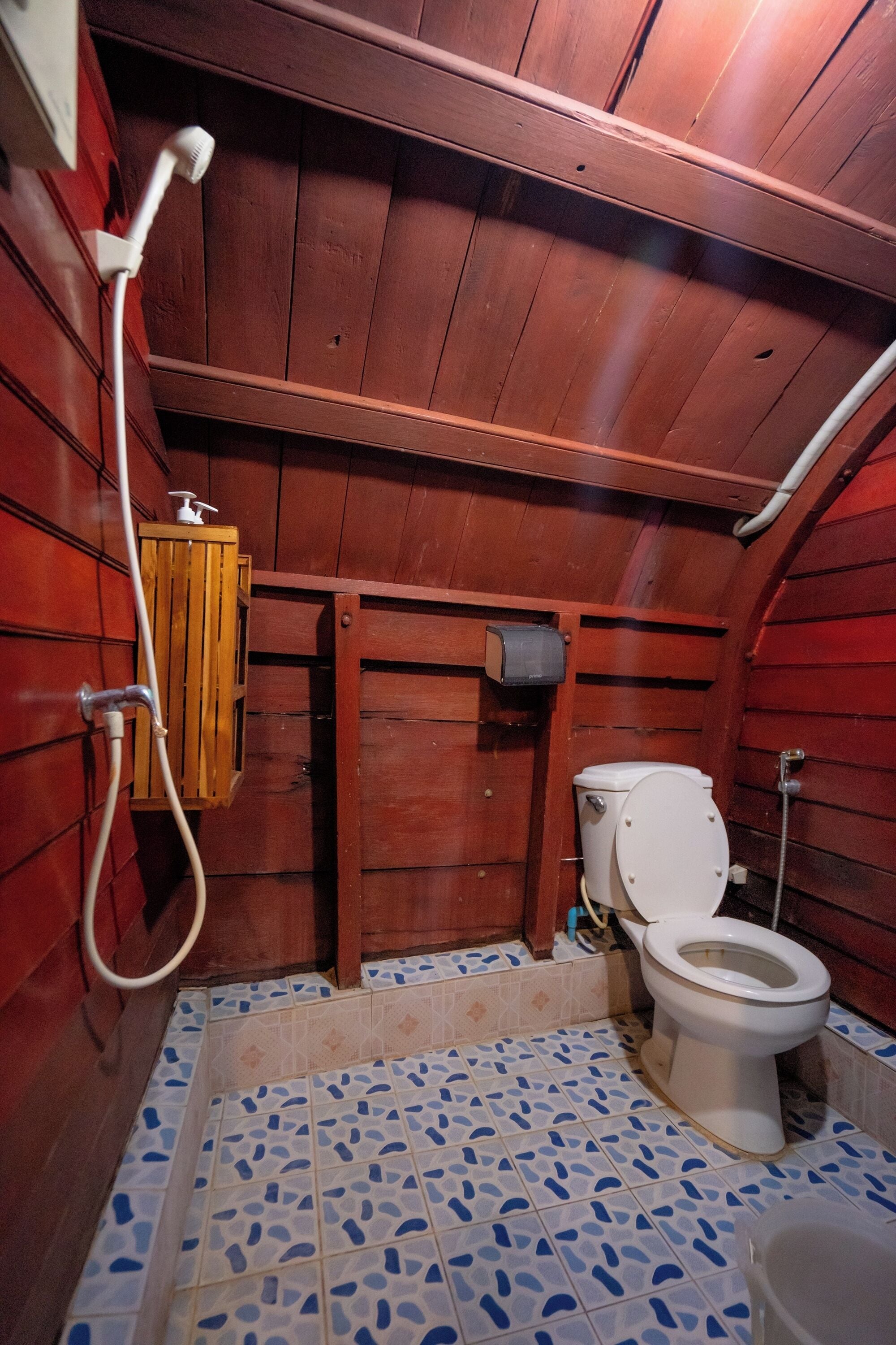 A small, wooden bathroom with a toilet, a shower, and a sink.
