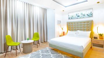 Een moderne hotelkamer met een groot bed, twee heldergroene stoelen, een klein rond tafeltje en een groot raam met gordijnen.