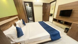 A hotel room with a large bed, a TV mounted on the wall, and a small seating area with a TV. - The Indian Hotel & Kitchen (Gurugram)