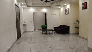 A hotel lobby with a tiled floor, a ceiling fan, a green chair, a black sofa, and a small table. - The Indian Hotel & Kitchen (Gurugram)