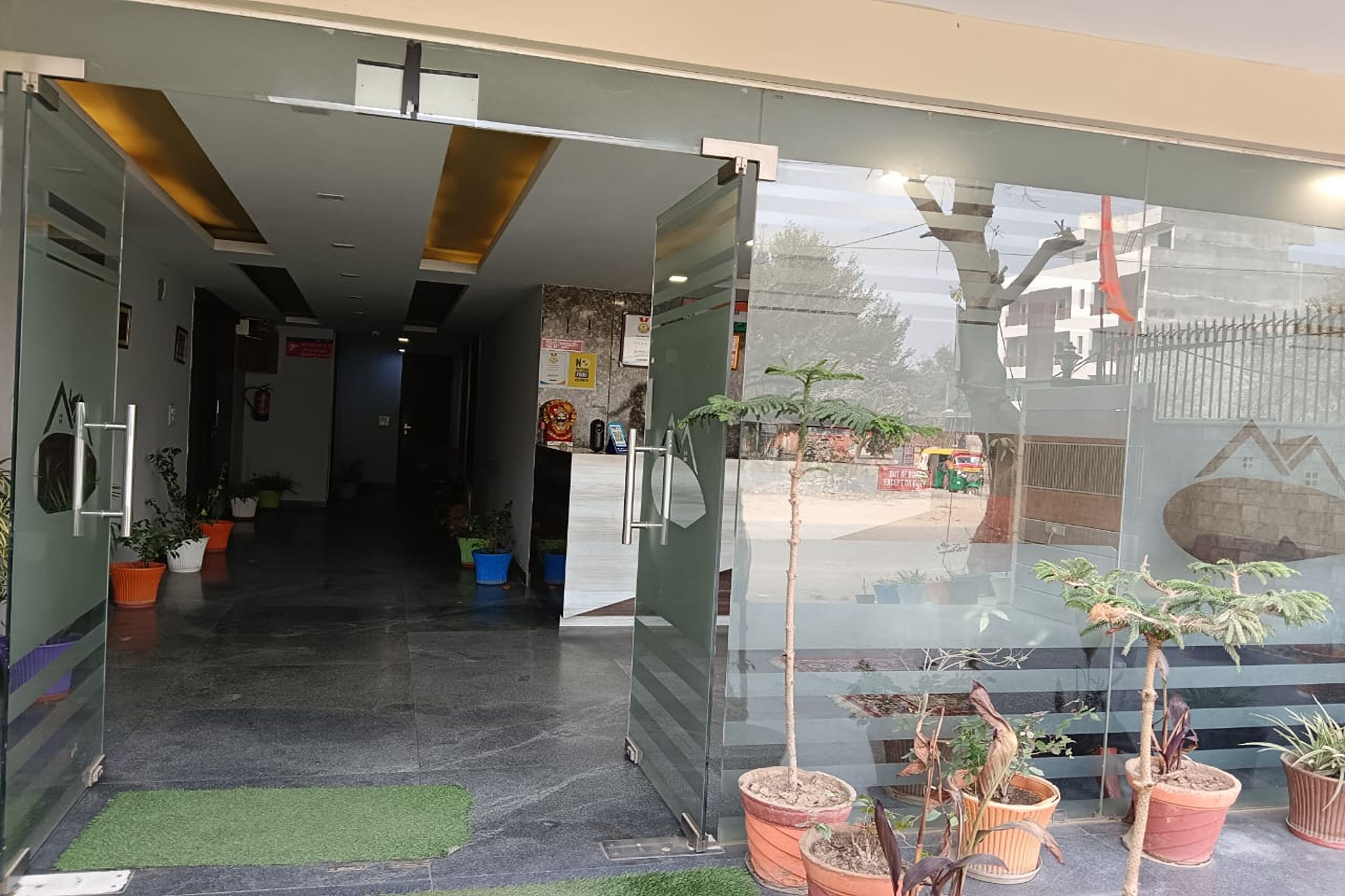 Zona de recepción con pared de vidrio, plantas en macetas y vistas al exterior.