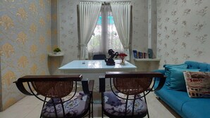 A room with a dining table, two chairs, a blue sofa, and a window with curtains. - R Residence (Medan)
