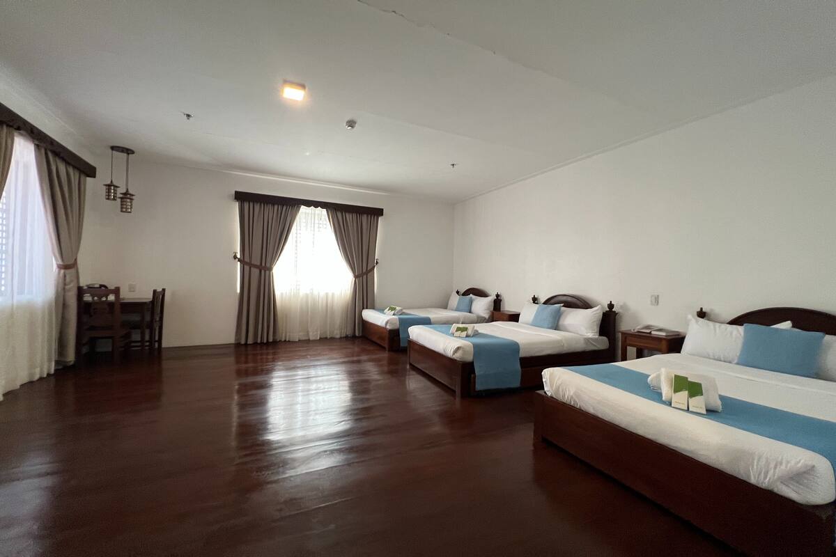 A hotel room with two beds, a dining table, and a window with curtains.