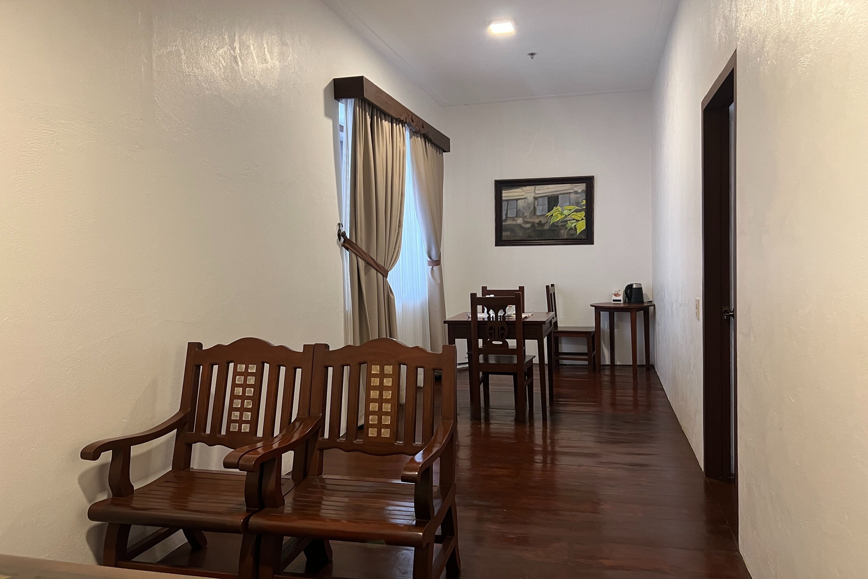 Un pasillo con sillas de madera, una mesa y un cuadro en la pared.