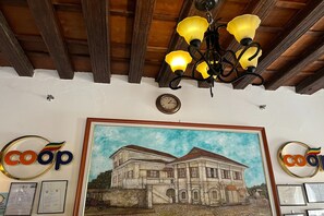 A hotel interior with a wooden ceiling, a chandelier, framed artwork of a building, and 'coop' signage. - Nscc Casa De Vigan (Vigan)