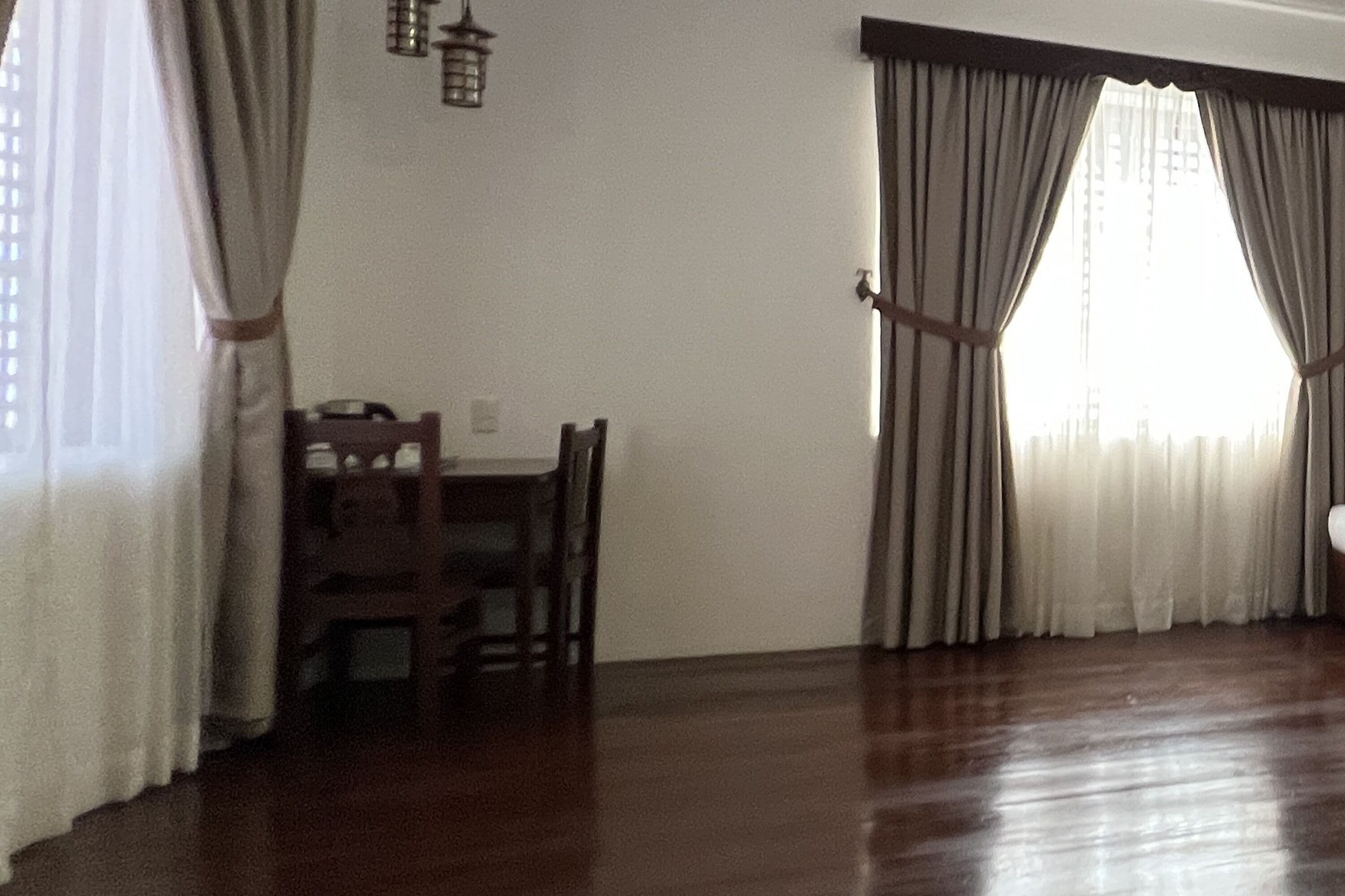 A room with a dining table and chairs, a window with curtains, and a wooden floor.