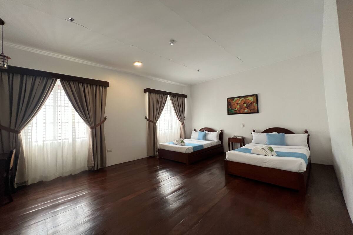 A hotel room with two beds, wooden flooring, and a painting on the wall.