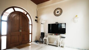 A room with a wooden door, a white desk with a television, and a decorative clock on the wall. - Clifton Villa (Mahabaleshwar)