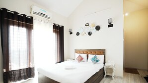 A neatly made bed with a wooden headboard, a bedside table, and a wall-mounted air conditioner. - Clifton Villa (Mahabaleshwar)