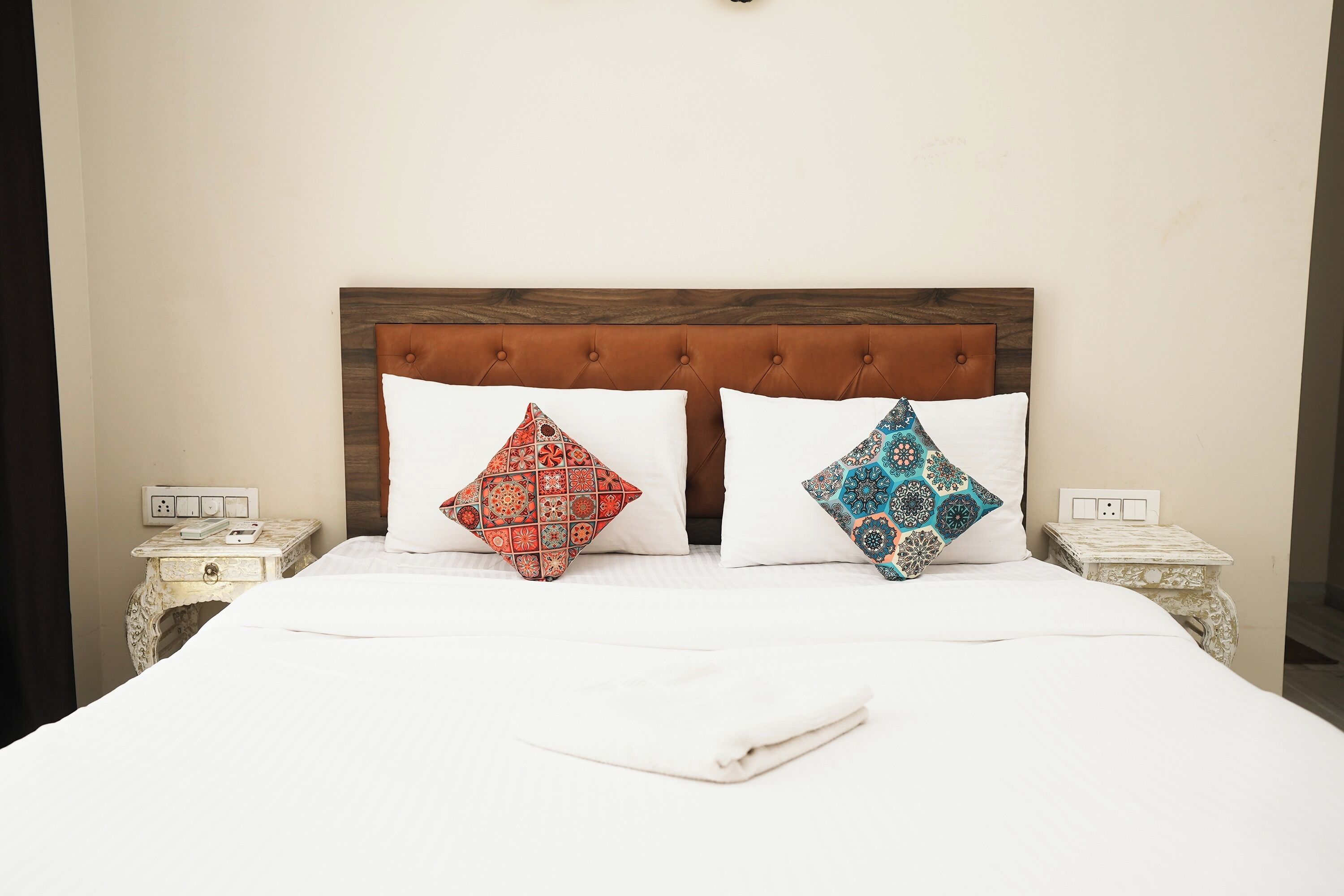 A bed with a wooden headboard, two patterned pillows, white bedding, and two bedside tables with a decorative design.