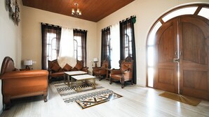 A spacious living room with a large wooden door, a sofa set, a coffee table, and a patterned rug. - Clifton Villa (Mahabaleshwar)
