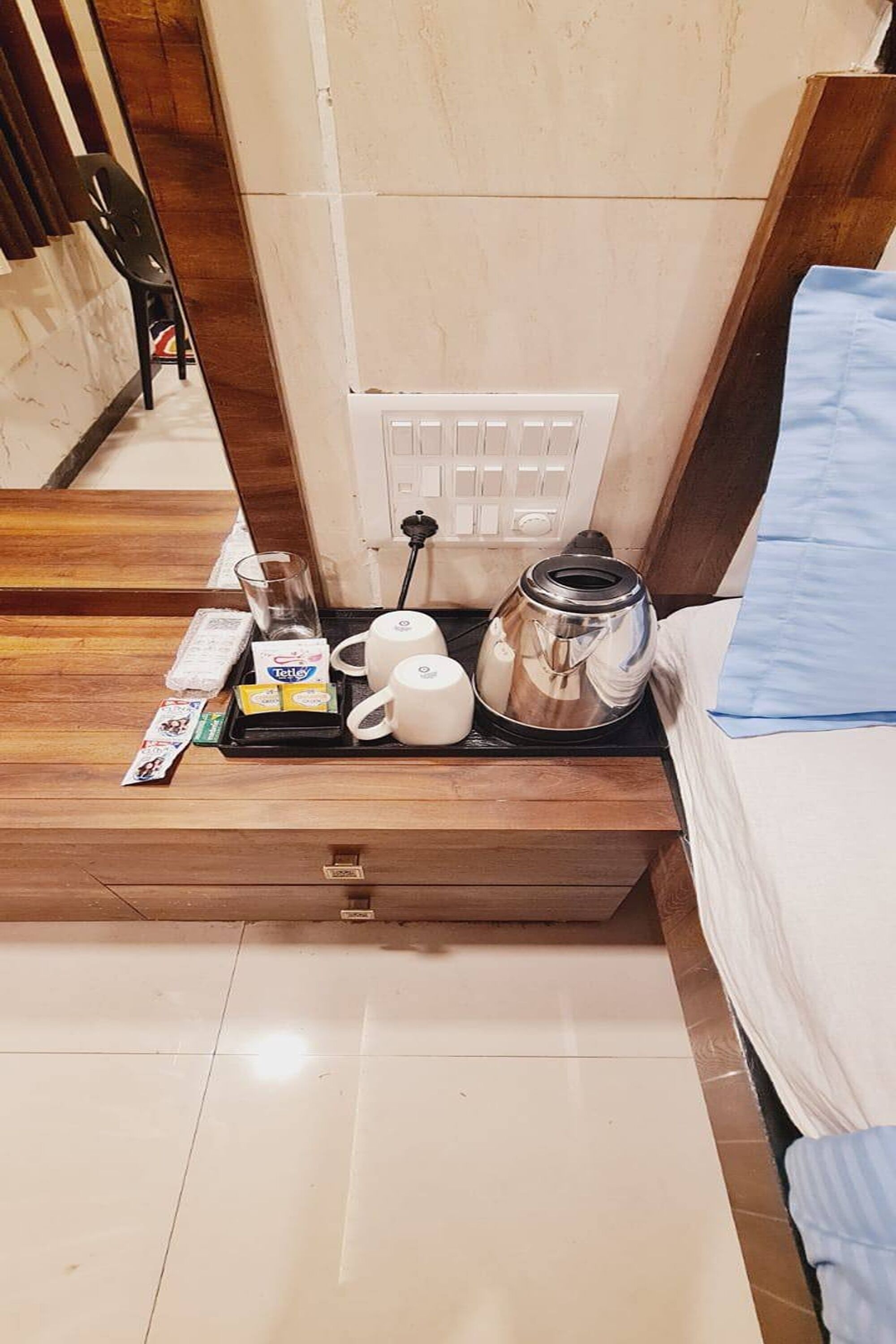 Une chambre d’hôtel avec une table de chevet en bois, une bouilloire, un verre et un plateau contenant des articles pour le petit-déjeuner.
